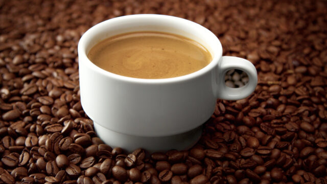 side view of white cup of black coffe on coffee beans